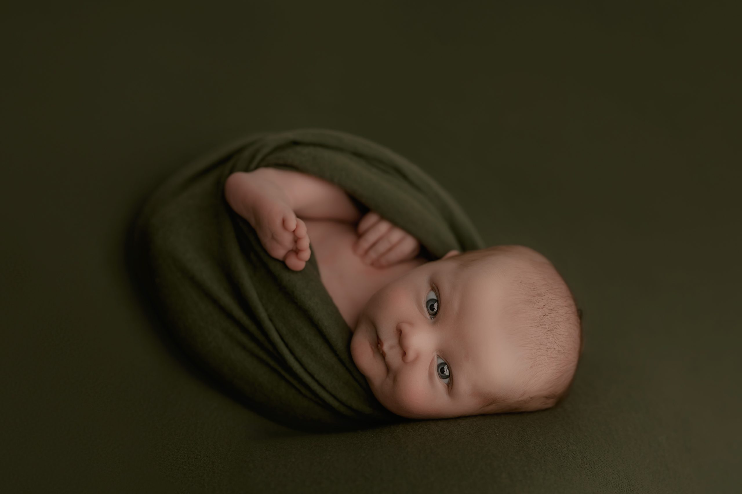 newborn baby on green backdrop looks into the camera