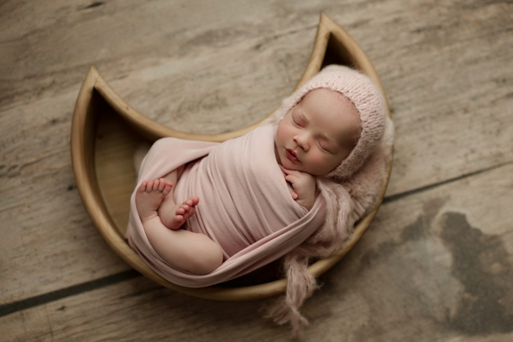 newborn baby girl wrapped in pink and sleeping in a moon shaped bowl