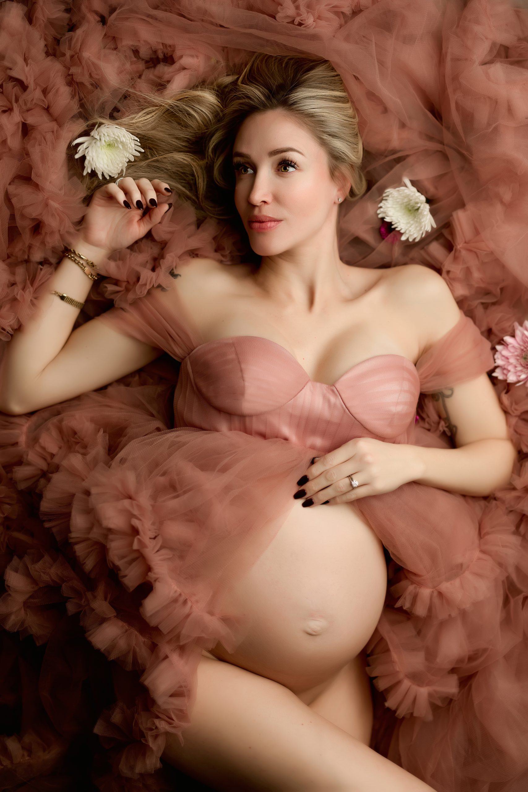 pregnant woman lays with pink ruffled tulle fabric and florals around her