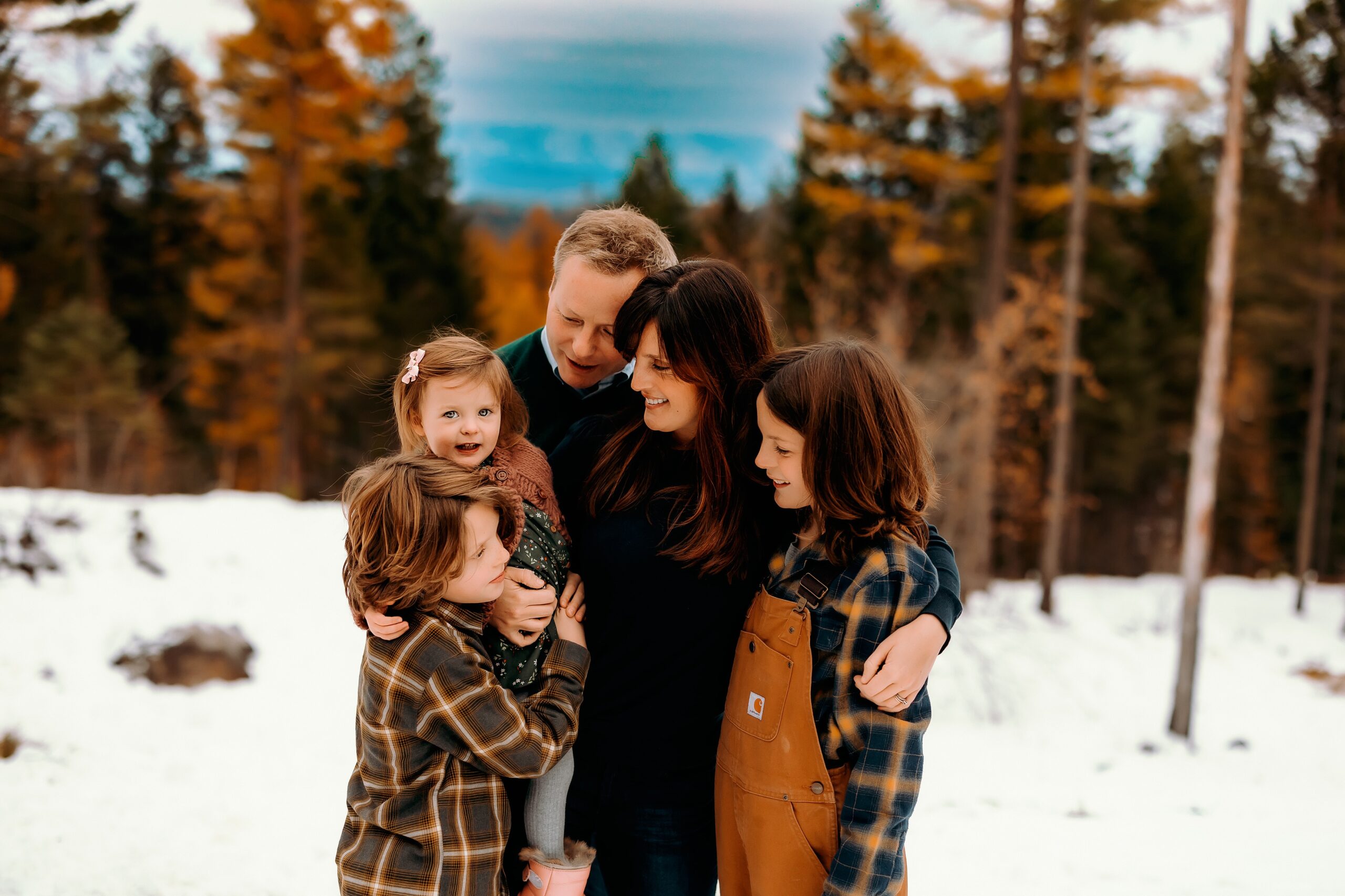 a family squeezes close together while laughing and smiling in the snow in whitefish, montana