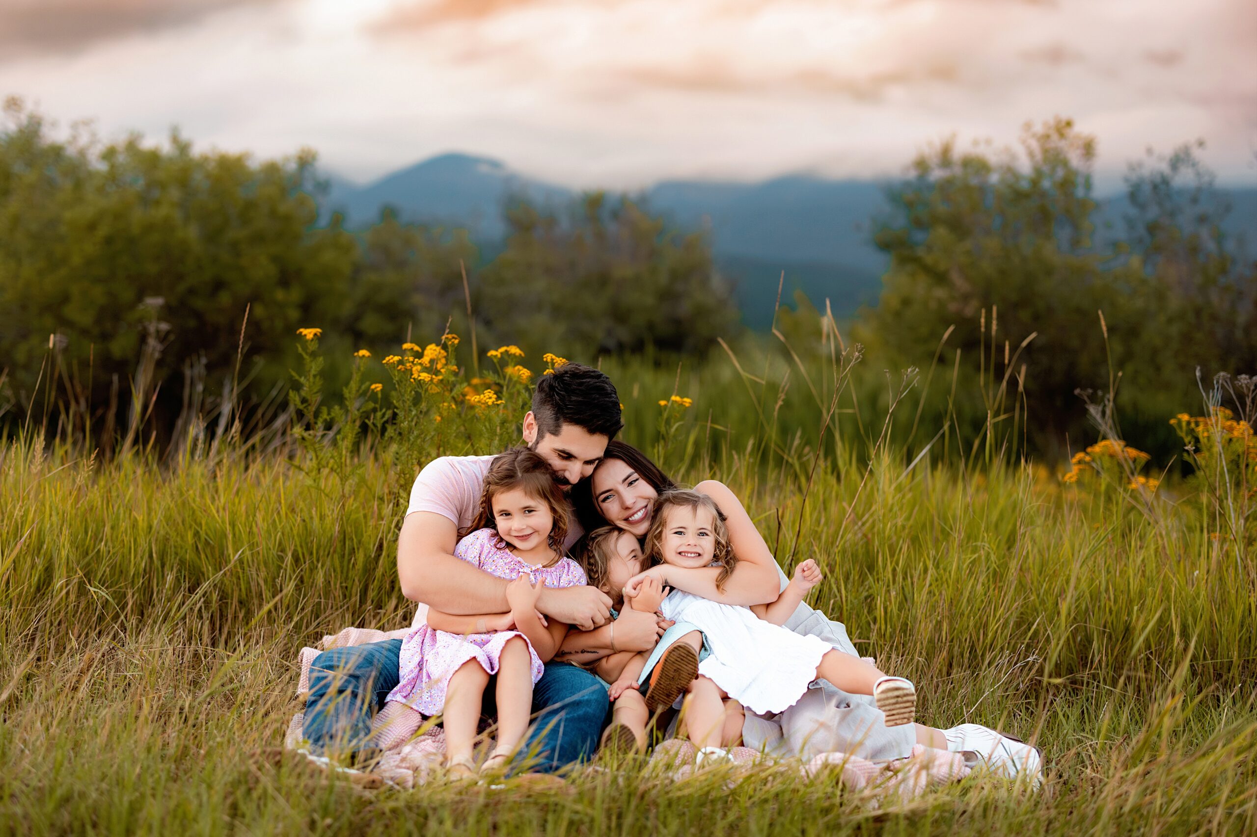 a family hugs in a green field in montana with a pink sunset in the background