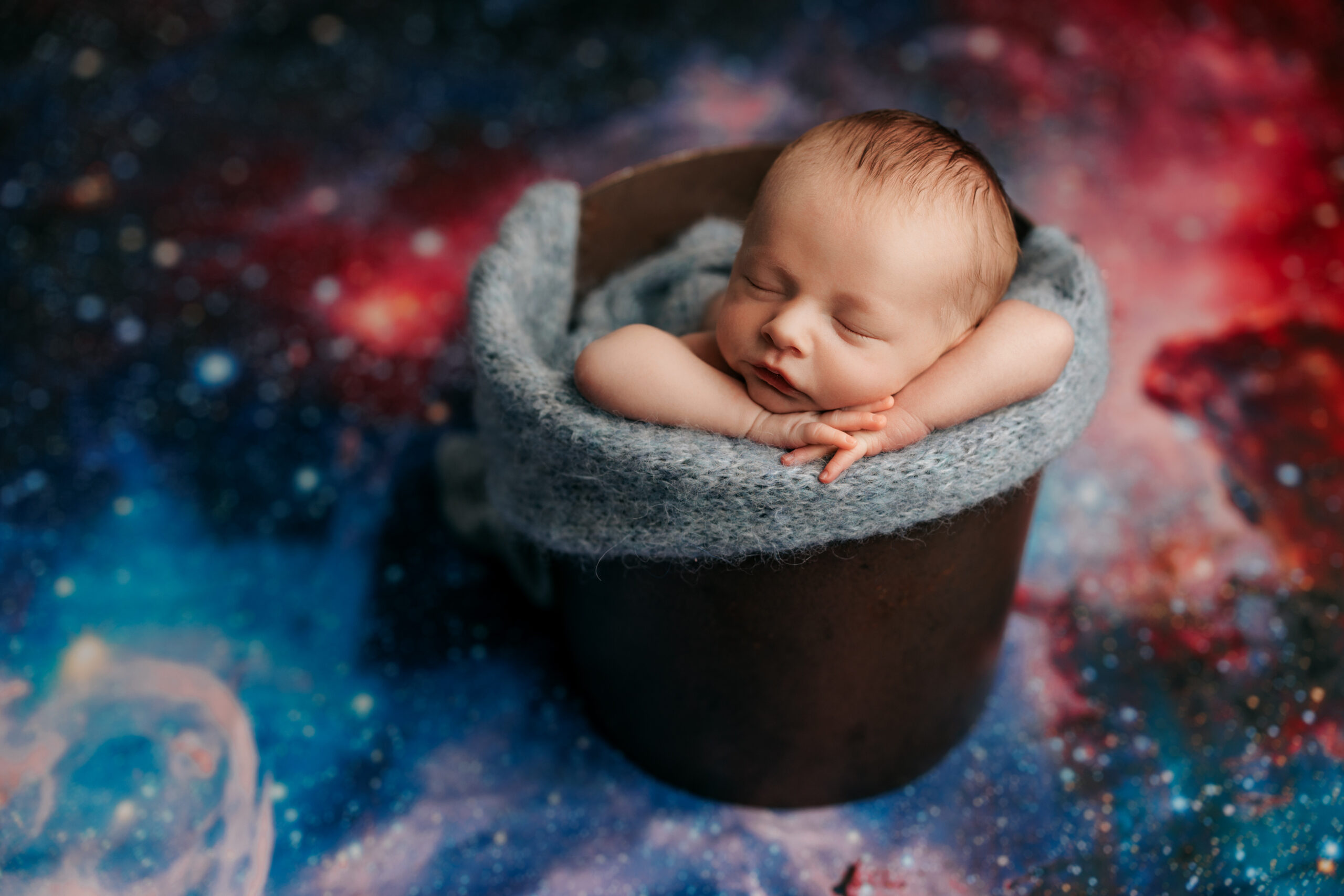 newborn baby boy posed in bucket with space blanket behind him